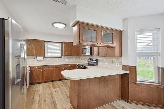 kitchen featuring kitchen peninsula, a wealth of natural light, light hardwood / wood-style flooring, and appliances with stainless steel finishes