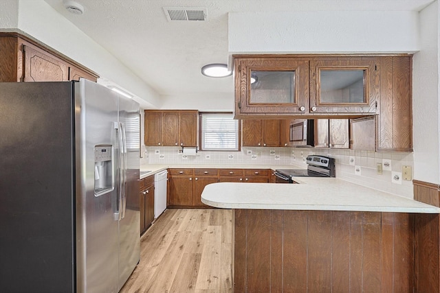 kitchen featuring light wood-type flooring, kitchen peninsula, stainless steel appliances, and tasteful backsplash