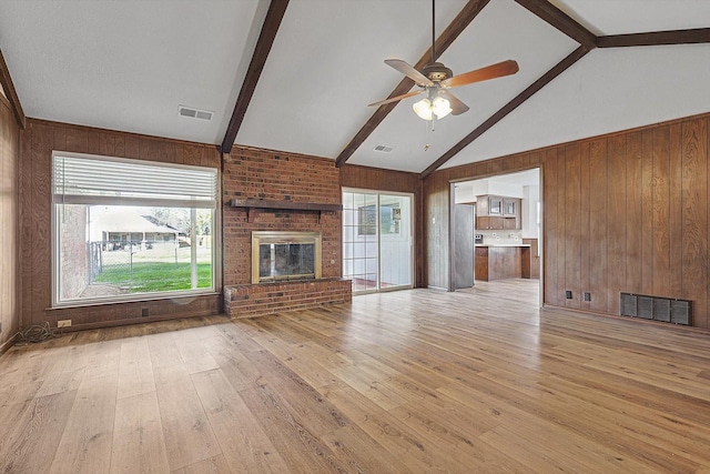 unfurnished living room featuring a fireplace, beam ceiling, light wood-type flooring, and wooden walls