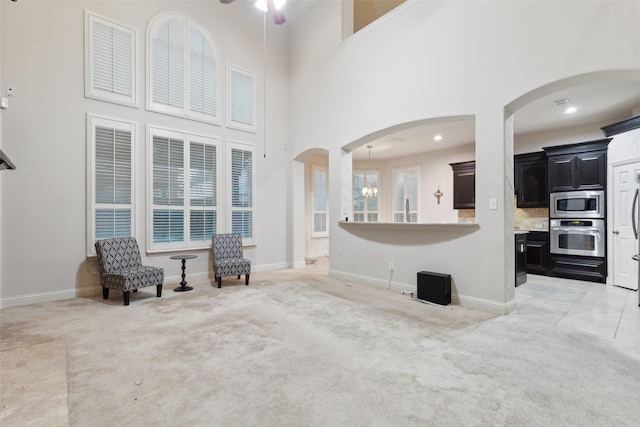 living area with a towering ceiling, ceiling fan with notable chandelier, and light colored carpet