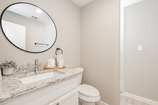 bathroom with vanity, wood finished floors, baseboards, visible vents, and toilet