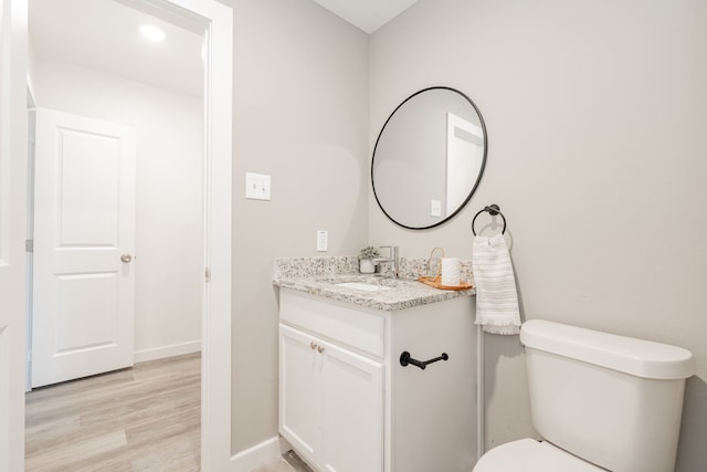 half bath featuring vanity, toilet, wood finished floors, and baseboards