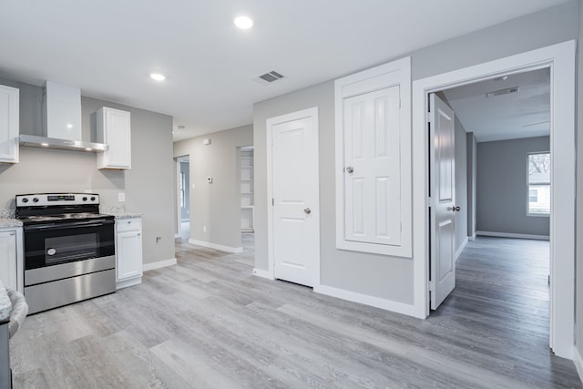 kitchen with electric stove, light hardwood / wood-style flooring, light stone countertops, white cabinets, and wall chimney exhaust hood