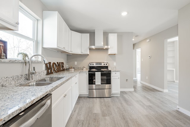 kitchen with light stone countertops, a sink, stainless steel appliances, white cabinets, and wall chimney range hood