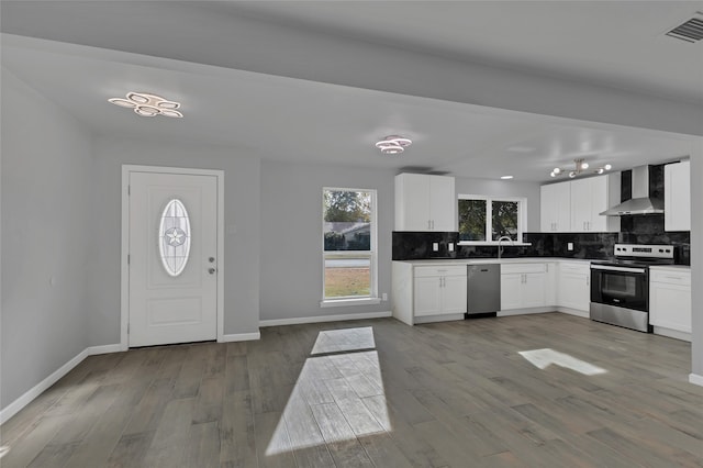 kitchen with white cabinetry, wall chimney range hood, stainless steel appliances, backsplash, and light hardwood / wood-style flooring