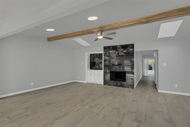 unfurnished living room with ceiling fan, vaulted ceiling with skylight, and a fireplace