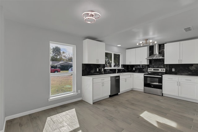 kitchen with white cabinets, a wealth of natural light, appliances with stainless steel finishes, and wall chimney exhaust hood