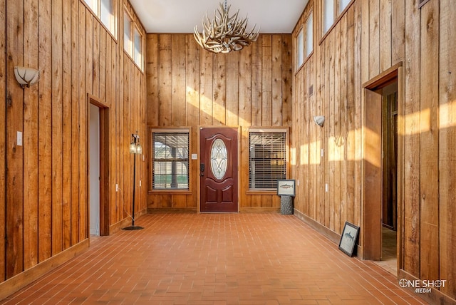 foyer entrance with a chandelier, a towering ceiling, and wooden walls