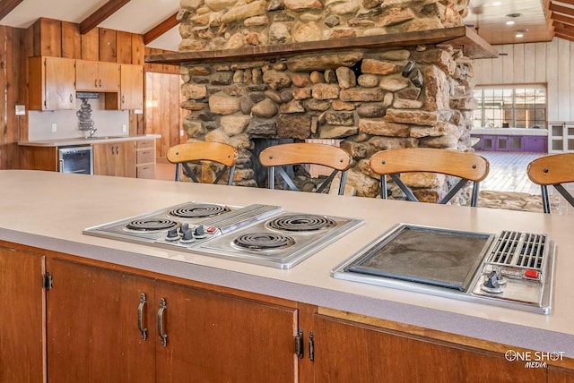 kitchen with a large fireplace, beverage cooler, lofted ceiling with beams, wood walls, and stainless steel cooktop