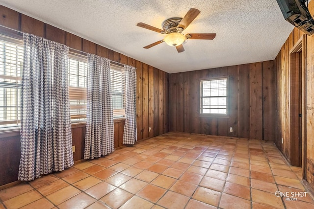 tiled spare room featuring wood walls, ceiling fan, and a healthy amount of sunlight