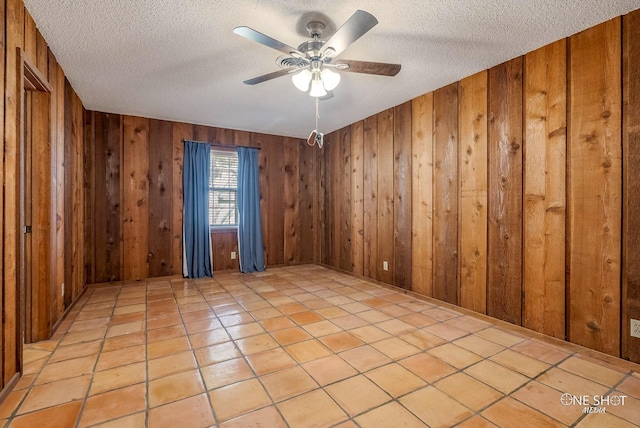 unfurnished room with light tile patterned floors, a textured ceiling, wooden walls, and ceiling fan