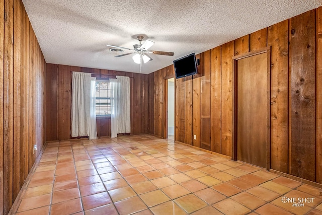 spare room featuring light tile patterned floors, a textured ceiling, wooden walls, and ceiling fan