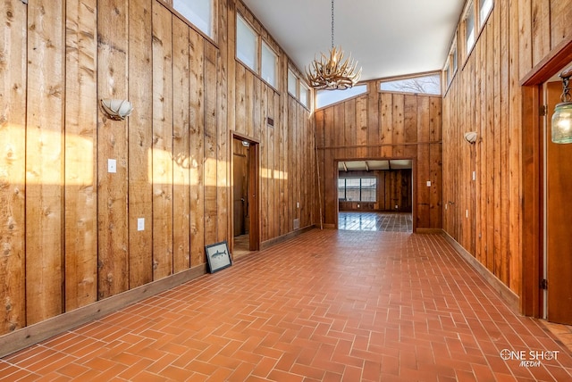 interior space with a towering ceiling, a notable chandelier, and wooden walls