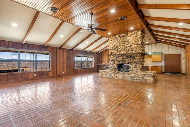 unfurnished living room featuring beam ceiling, a stone fireplace, ceiling fan, and wood walls