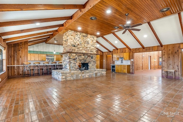 unfurnished living room with ceiling fan, beam ceiling, high vaulted ceiling, a fireplace, and wood walls