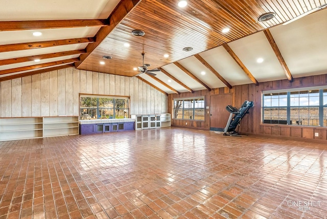 unfurnished living room with a healthy amount of sunlight, wood walls, ceiling fan, and lofted ceiling with beams