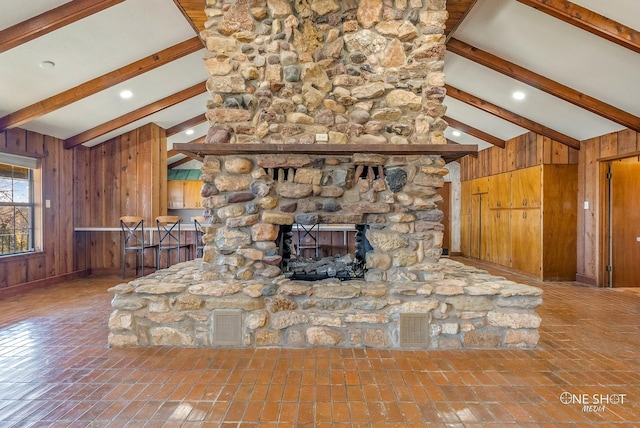 unfurnished living room with lofted ceiling with beams, a stone fireplace, and wooden walls