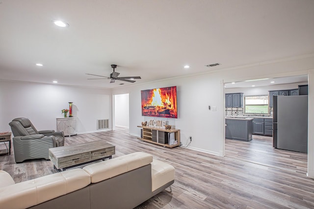 living room with ornamental molding, sink, ceiling fan, and light hardwood / wood-style flooring