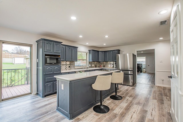 kitchen featuring stainless steel refrigerator, built in microwave, tasteful backsplash, a center island, and light hardwood / wood-style floors