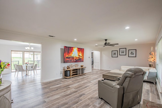 living room with ceiling fan with notable chandelier, light hardwood / wood-style floors, and ornamental molding