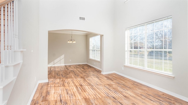 spare room with hardwood / wood-style flooring, a towering ceiling, and an inviting chandelier