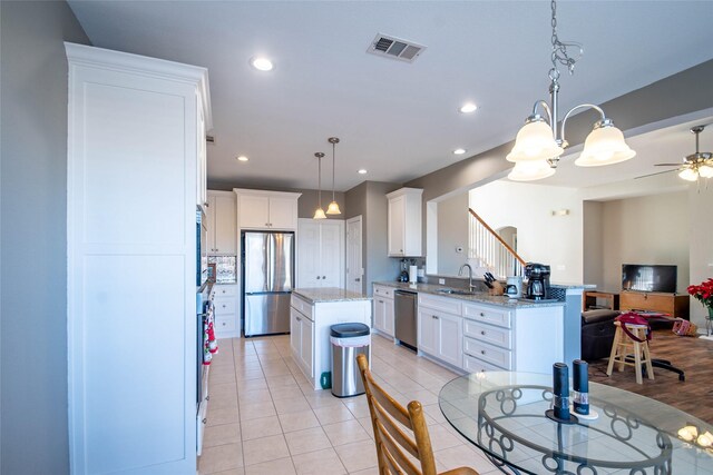 kitchen featuring sink, hanging light fixtures, a kitchen island, white cabinets, and appliances with stainless steel finishes