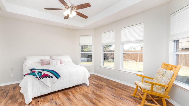 bedroom with wood-type flooring, a raised ceiling, and ceiling fan