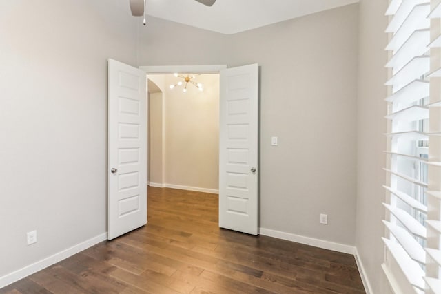 unfurnished bedroom with ceiling fan with notable chandelier and dark hardwood / wood-style flooring