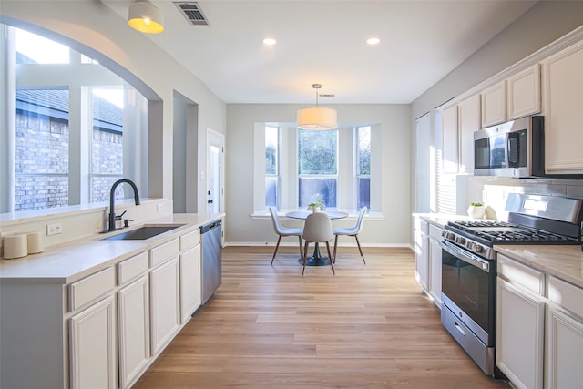 kitchen featuring light wood-type flooring, stainless steel appliances, sink, pendant lighting, and white cabinetry