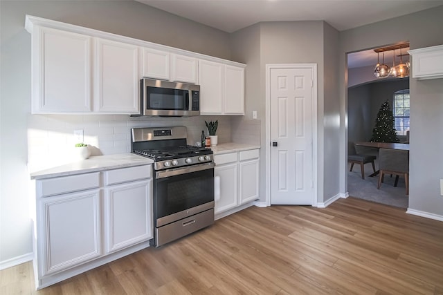 kitchen featuring decorative backsplash, white cabinets, stainless steel appliances, and decorative light fixtures