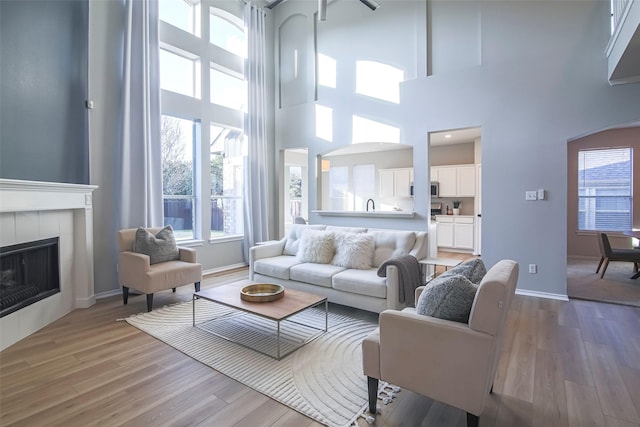 living room with a tiled fireplace, wood-type flooring, and a high ceiling