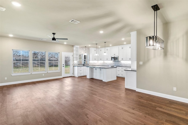 kitchen featuring dark hardwood / wood-style flooring, ceiling fan with notable chandelier, pendant lighting, white cabinets, and a kitchen island