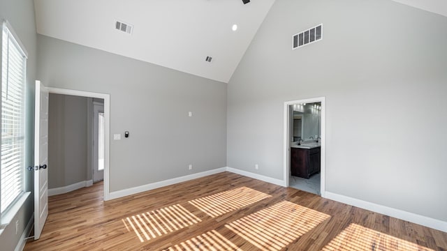 unfurnished bedroom featuring connected bathroom, high vaulted ceiling, multiple windows, and light wood-type flooring