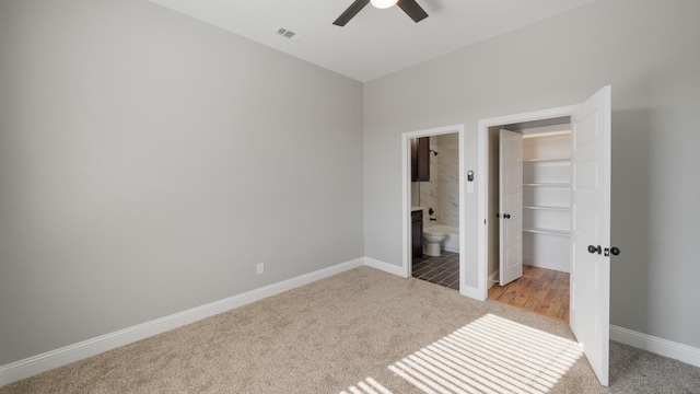 unfurnished bedroom featuring ceiling fan, light colored carpet, a closet, and ensuite bath