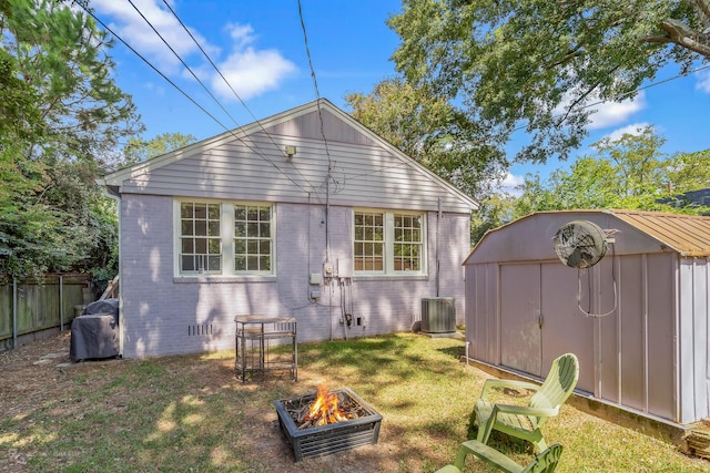 rear view of property with central AC unit, a storage unit, an outdoor fire pit, and a lawn