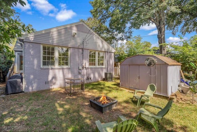 rear view of house with an outdoor fire pit, a storage shed, and a lawn