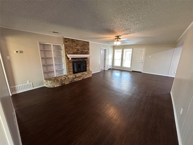 unfurnished living room with built in features, dark hardwood / wood-style flooring, ornamental molding, a brick fireplace, and a textured ceiling