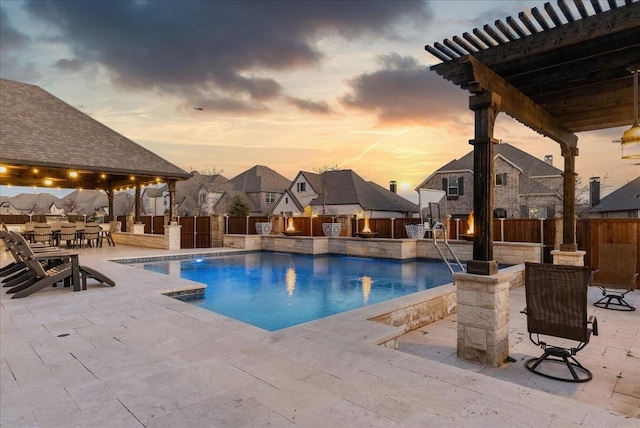 pool at dusk featuring exterior fireplace, a patio area, and an outdoor bar