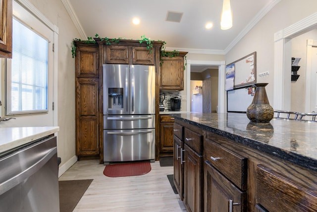 kitchen with dark stone countertops, backsplash, stainless steel appliances, crown molding, and light hardwood / wood-style flooring