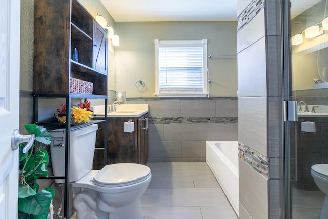 bathroom with a tub to relax in, toilet, tile walls, vanity, and tile patterned flooring