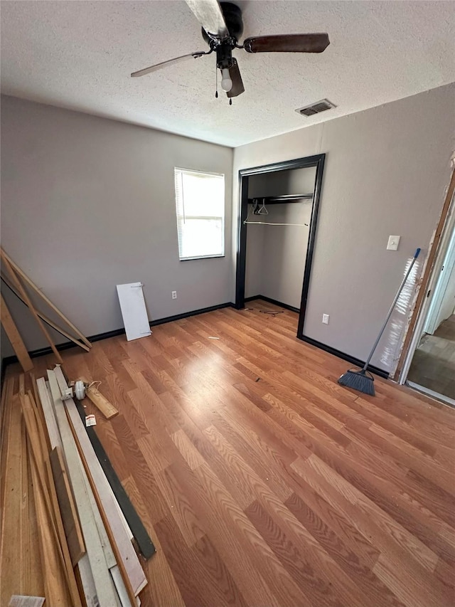 unfurnished bedroom with ceiling fan, a closet, a textured ceiling, and light wood-type flooring