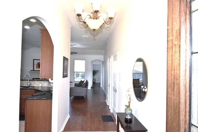 corridor with dark wood-type flooring, sink, and an inviting chandelier