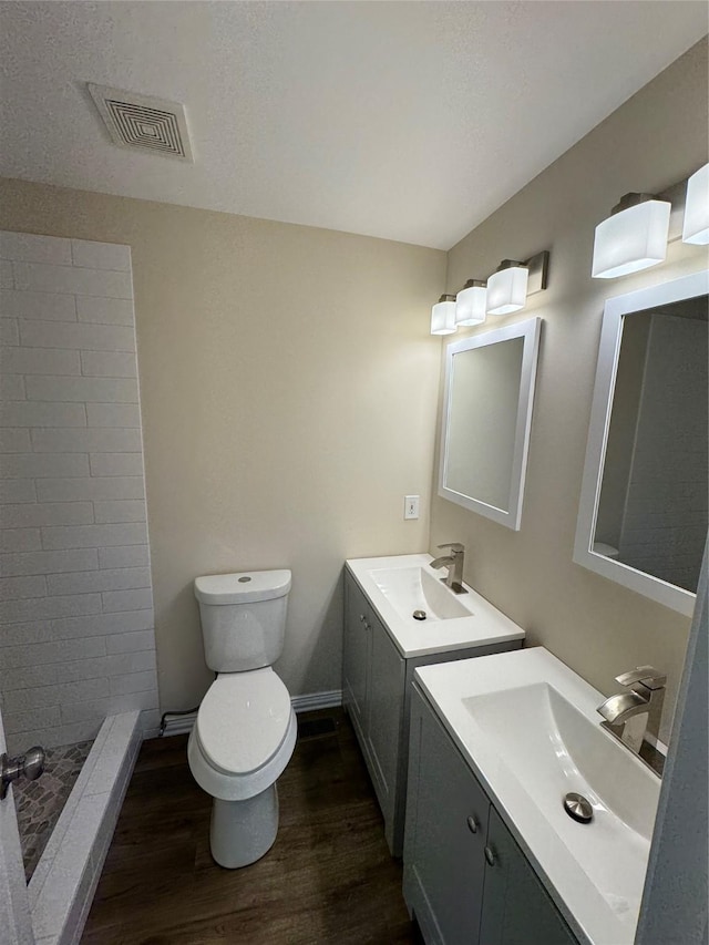 bathroom featuring vanity, toilet, hardwood / wood-style floors, and a tile shower