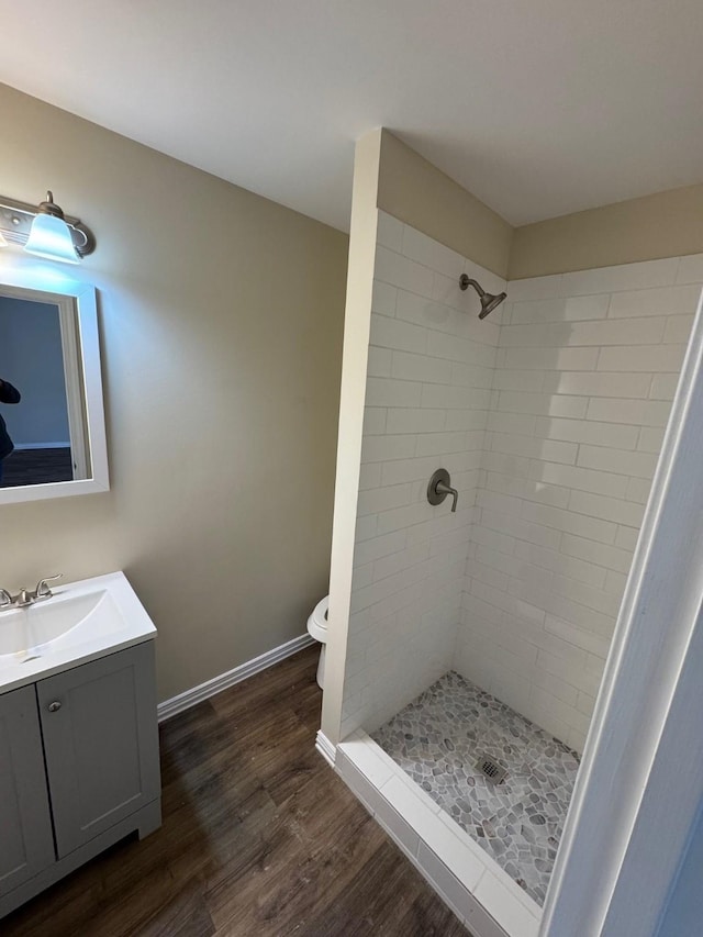 bathroom with a tile shower, hardwood / wood-style floors, vanity, and toilet