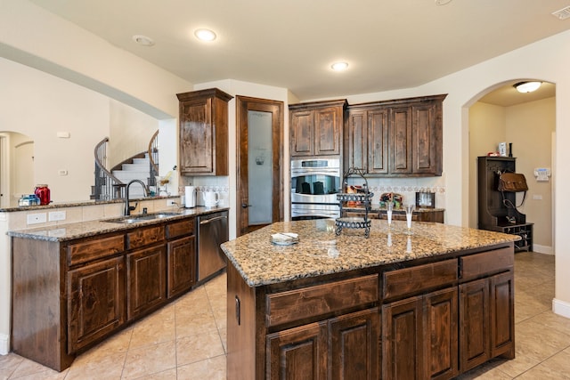 kitchen featuring sink, a kitchen island with sink, stainless steel appliances, light stone counters, and tasteful backsplash