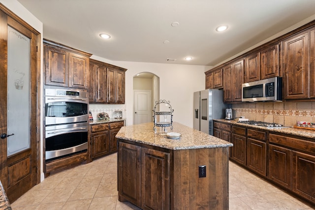 kitchen with light stone counters, dark brown cabinetry, stainless steel appliances, and a kitchen island