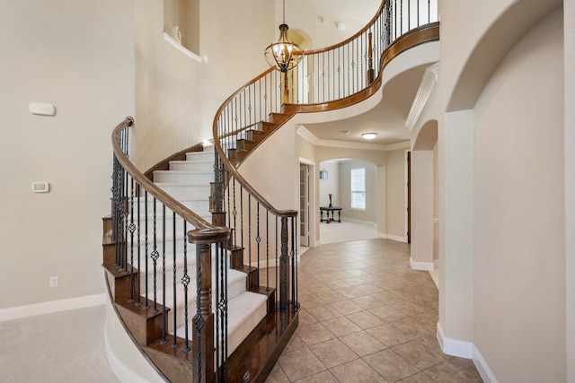 tiled foyer entrance featuring ornamental molding, a towering ceiling, and an inviting chandelier