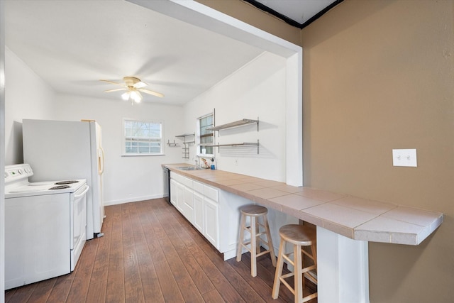 kitchen featuring a breakfast bar, white electric stove, sink, white cabinets, and tile counters