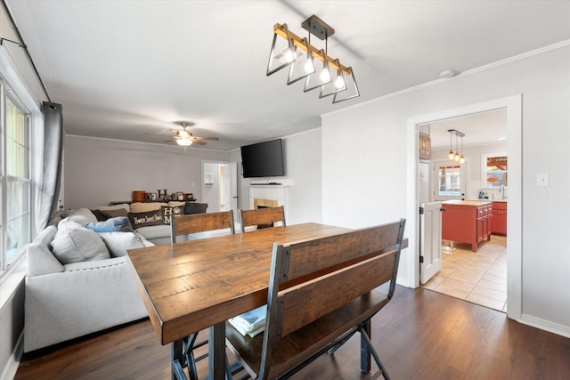 dining space with crown molding, hardwood / wood-style flooring, a tile fireplace, and ceiling fan