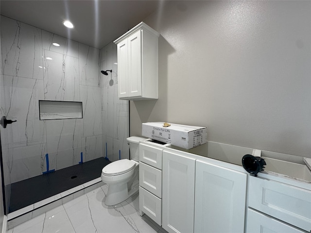 bathroom featuring a tile shower, vanity, washer / clothes dryer, and toilet